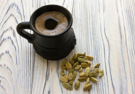 Arabic coffee in black ceramic cup and cardamom granules on light gray wooden background.