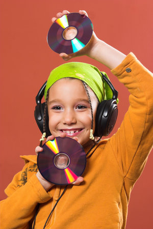 little pretty child listening music in headphones and holding two CD