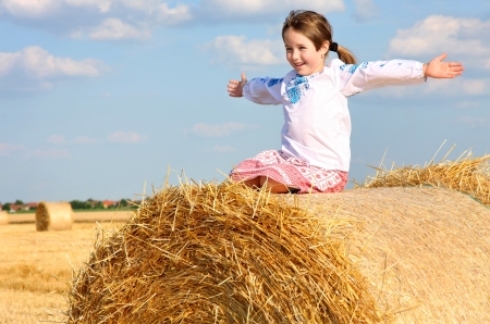 small rural girl on the straw after harvest field with straw balesの写真素材