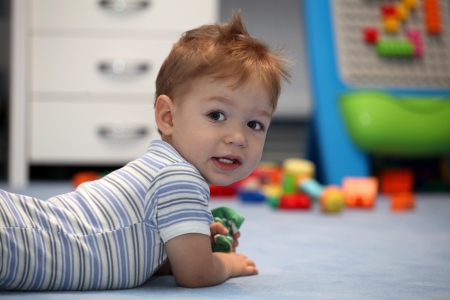 A happy baby boy lying on a floor in children's roomの写真素材