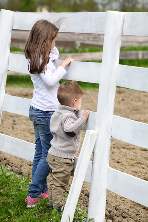 Pre-teen girl and Baby boy on the a white picket fence beside the horseの写真素材