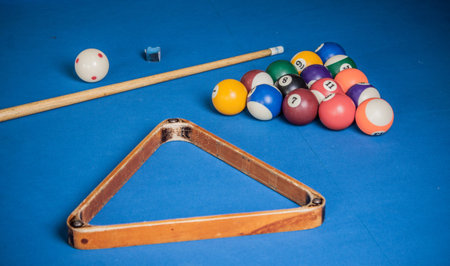 Billiard balls, cue and chalk on a blue pool table..