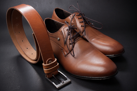Selective focus of men's leather belt and shoe on wooden table.の写真素材
