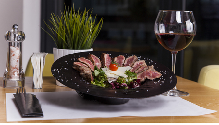 Juicy rib eye beef steak medium rare with spices cut in slices on slate plate with fried garlic and spinach salad. dark style, view from above, close-up.の写真素材
