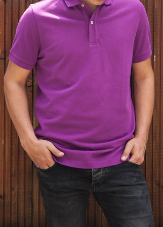 Young Beautiful male model in purple polo T-shirt and dark black and blue jeans on brown wooden background.の写真素材