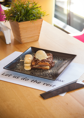 Chocolate Waffle topped with ice cream and banana decoration on black plate.の写真素材