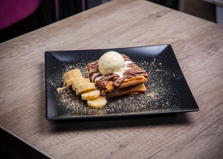 Chocolate Waffle topped with ice cream and banana decoration on black plateの写真素材