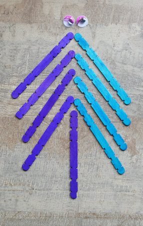 Creative festive concept: a Christmas tree made of purple and blue wooden sticks, with two funny...