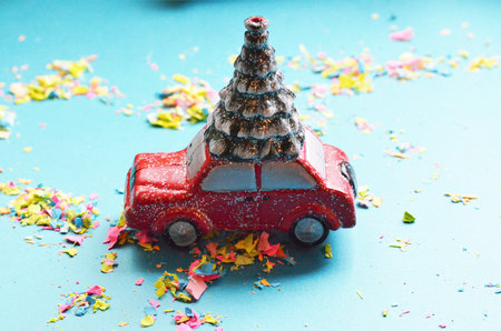 Christmas concept: a red car carrying a Christmas tree, on a blue background with confetti