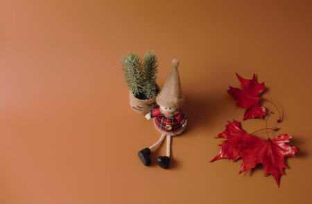 Winter concept: a snowman sitting by a Christmas plant in a pot and some red fallen leaves.