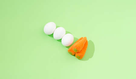 2021 Easter minimal composition. Three white eggs and three carrots on a pastel green background. Minimal creative flat lay composition.の写真素材