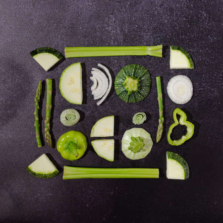 A spring or summer infographic made of green vegetables: celery, asparagus, onions, zucchini, paprika, on black background. Healthy green food concept. Vegetarian artistic background. Flat lay.の写真素材