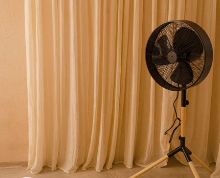 A big black fan standing in front of beige curtains. Minimal summer heat composition. Retro air condition conceptの写真素材