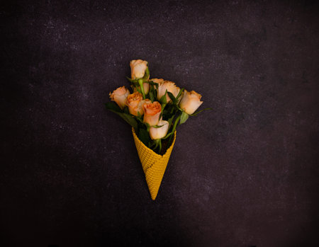 A beautiful bouquet of orange roses emerging from a bright yellow cone on a dark marbled background. Dreamy romantic summer present concept. Trendy vibrant yellow design.の写真素材