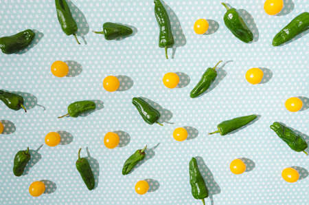 A bright pattern made of green paprika and yellow cherry tomatoes on a squared blue-green background. Cheerful fresh vitamins creative design.の写真素材