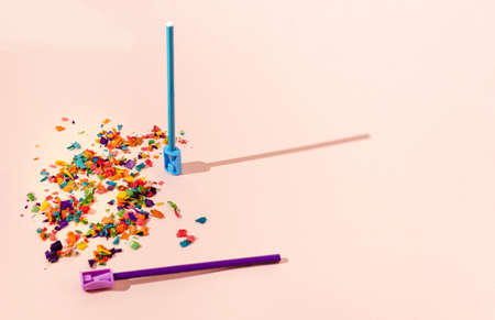 A blue and a violet pencil with sharpeners in the same color, pencil shavings, on a peach background. School year or education for all children creative concept.の写真素材