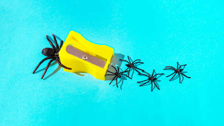 A big black spider entering in a pencil sharpener, four small spiders falling out like shavings. Surreal Halloween vibes. Banner or party invitation.の写真素材