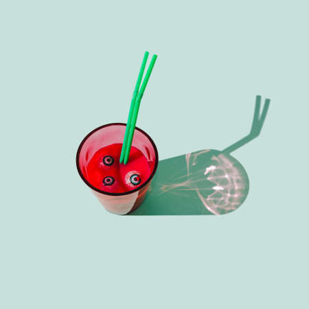 A glass filled with red drink, with eye balls in the liquid and two green straws. Pastel mint background. Spooky Halloween traditional celebration concept.の写真素材