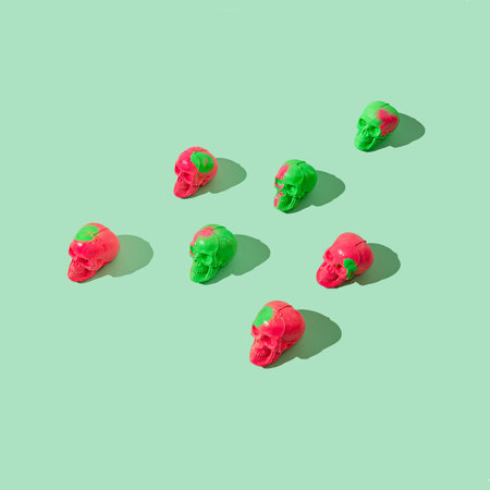 A pattern made of green and fuchsia sculls on a pastel green background. Creative Halloween or Day...