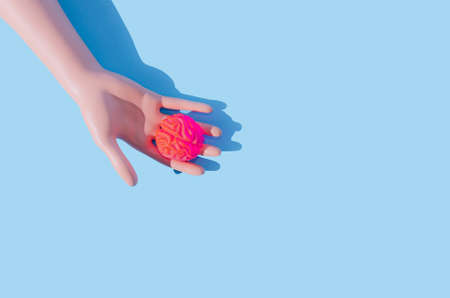 A woman's hand holding a neon pink human brain. Pastel blue background. Spooky Halloween creative concept. People with brain or brainless people creative design.の写真素材