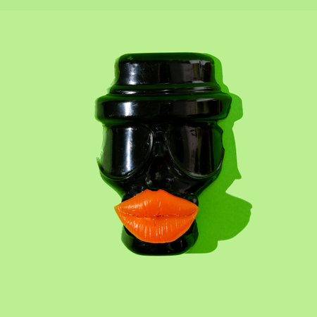A black scull wearing a hat and with bright orange lips on neon green background. Halloween party invitation concept. Spooky artistic design for banner or advertisement.の写真素材