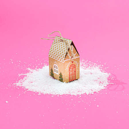 A cute house on snow, pastel pink background. Surreal winter season creative concept. Christmas or New Year atmosphere banner or card design.の写真素材