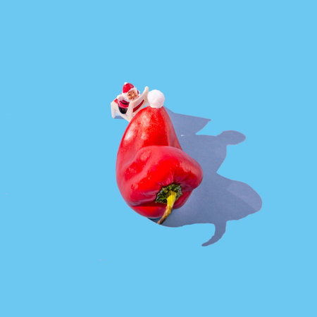 A small Santa Claus on a chair trying to get a white pompom from a big red paprika. Surreal funny...