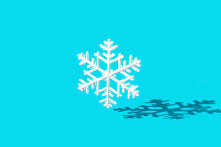 A big white snowflake falling on a pastel blue background with a strong shadow. Minimal winter season creative design. Banner or advertising for Christmas or New Year festivities.の写真素材