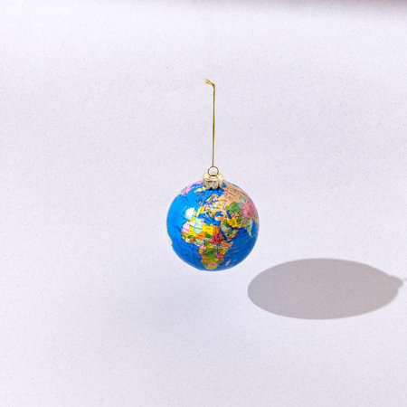 A globe hanging like a Christmas ball on light grey background. Surreal Christmas or New Year...
