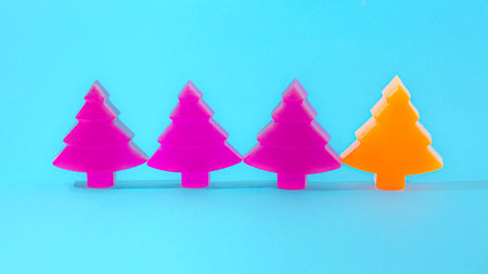 Three purple Christmas trees and one orange neatly alligned on pastel blue background. Minimal...