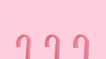 Three Christmas candy sticks on pastel pink background with copy space. Flat lay. Creative design for festive card or web banner or advertisement.の写真素材
