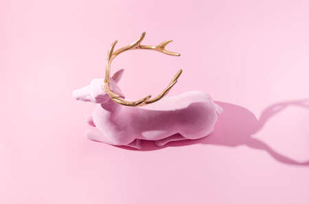 A pink reindeer with golden horns  on pastel pink background. Minimal winter festive season creative concept for web banner or card. Surreal traditional Christmas or New Year symbolic design.の写真素材