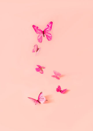 Pink butterflies flying over a pastel pink background. Romantic spring wallpaper with copy space.の写真素材