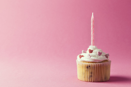 One nicely decorated muffin with cream, sprinkles and birthday candle isolated on pink backgroundの写真素材