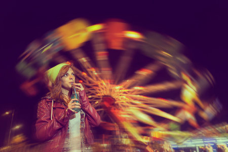 Beautiful young girl having fun and drinking juice at theme park