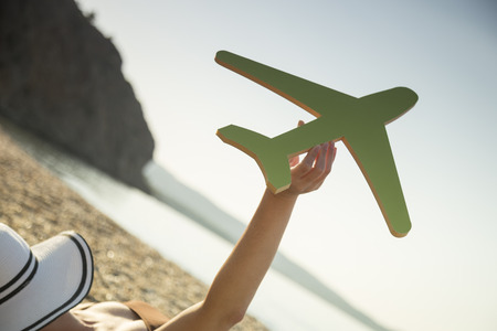 Female hand holding a cardboard airplane with the seascape in the background. Summer vacations transportation advertisementの写真素材