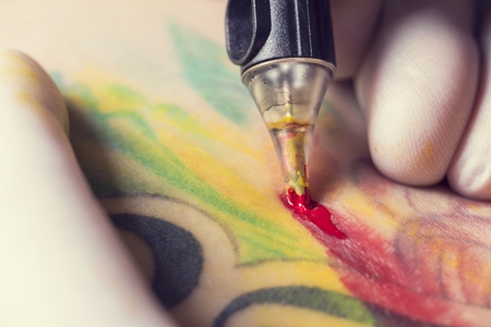 Male tattoo artist showing the process of making a tattoo on arm. Colorful tattoo art on human body and skin. Tattooist holding an active machine or gun.の写真素材