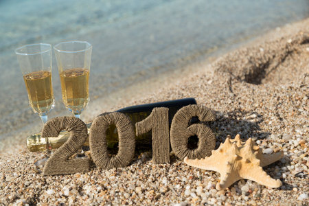 Champagne bottle lying on the beach with two champagne glasses, starfish and cardboard numbers 2016...