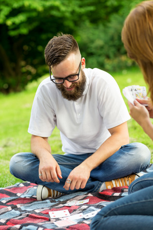 Couple in love on a picnic in nature, sitting on a picnic plaid, playing a card game and having funの写真素材