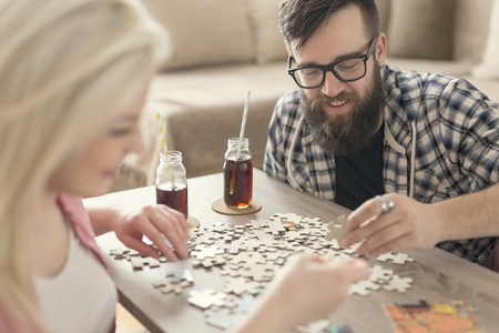 Couple in love sitting on the floor next to a table, solving a jigsaw puzzle problem and enjoying their leisure time activities.の写真素材