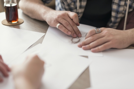 Young couple in love sitting on the floor next to the table, holding drawing charcoals and sketching on the empty sheets of paper.Leisure time activities,relaxation and spending quality time togetherの写真素材