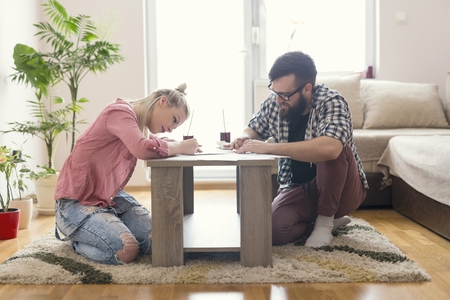 Young couple in love sitting on the floor next to the table, holding drawing charcoals and sketching on the empty sheets of paper.Leisure time activities,relaxation and spending quality time togetherの写真素材