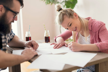 Young couple in love sitting on the floor next to the table, holding drawing charcoals and sketching on the empty sheets of paper.Leisure time activities,relaxation and spending quality time togetherの写真素材