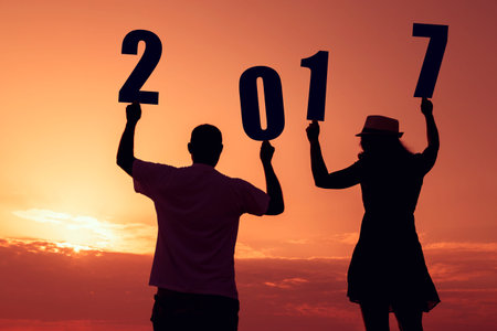 Silhouette of a couple in love standing on a rocky shore, holding numbers 2017 and looking at a...