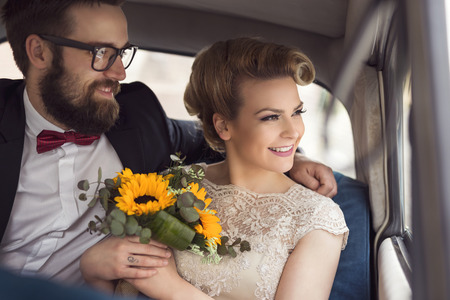 Young newlywed couple sitting in a retro vintage car, hugging and going away on a honeymoonの写真素材