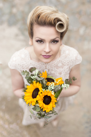 Top view of a beautiful young bride in a wedding dress, standing on a cobble road and holding a sunflower bouquetの写真素材