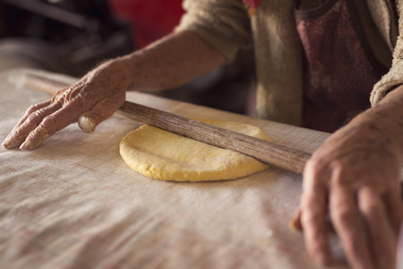 Detail of an elderly woman's hand rolling out a dough with a rolling pin while making homemade pasta. Selective focusの写真素材