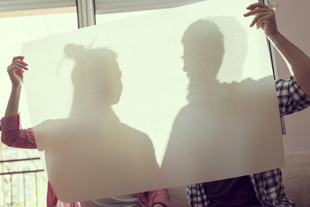 Couple in love standing next to a window behind a big piece of tracing paper while their visible silhouettes are about to kiss each otherの写真素材