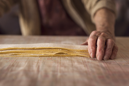 Detail of an elderly woman's wrinkled hand holding stripes of dough for preparation of homemade pastaの写真素材
