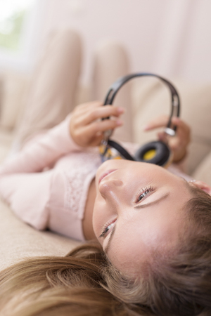 Young attractive woman lying on a couch in the living room, wearing a headset, listening to the music and enjoying her freedom and leisure timeの写真素材